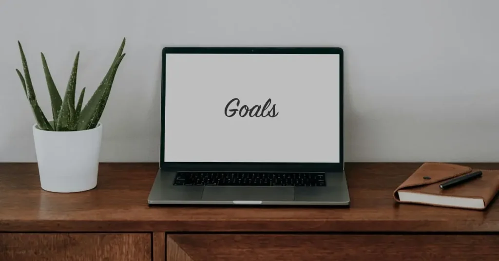 una laptop con la palabra "goals" en el medio con un fondo minimalista, que refleja las metas que debe tener una empresa al contactarse con una Agencia de Publicidad para que se encargue de su gestión de redes sociales